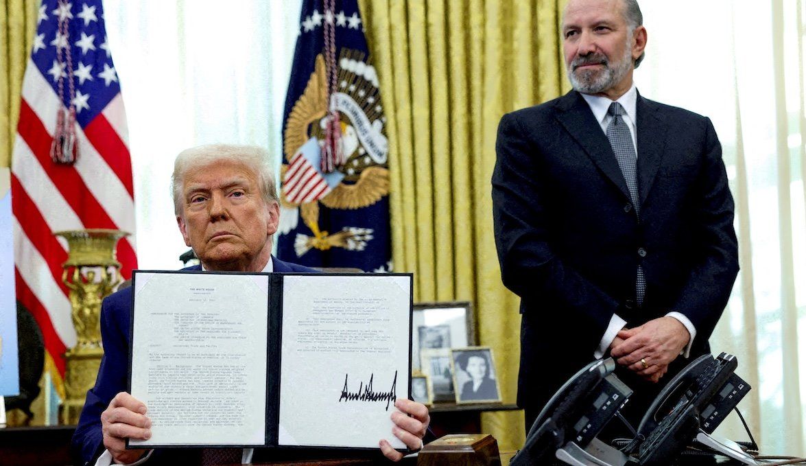 President Donald Trump holds an executive order about tariffs while flanked by Commerce Secretary Howard Lutnick in the Oval Office on Feb. 13, 2025. 