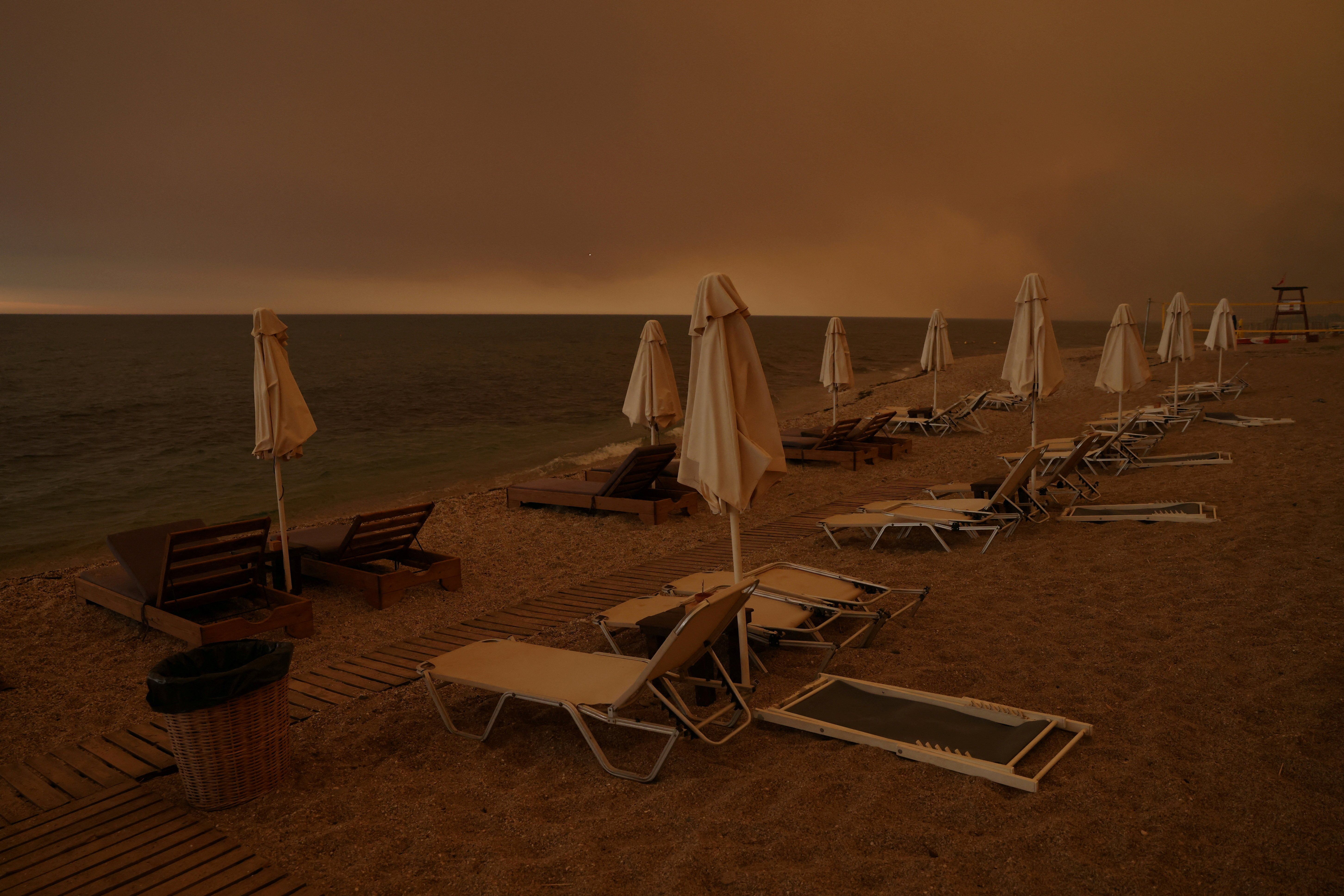 Smoke rises next to sunbeams and umbrellas as a wildfire burns, at the beach of the village of Dikella in the region of Evros, Greece.