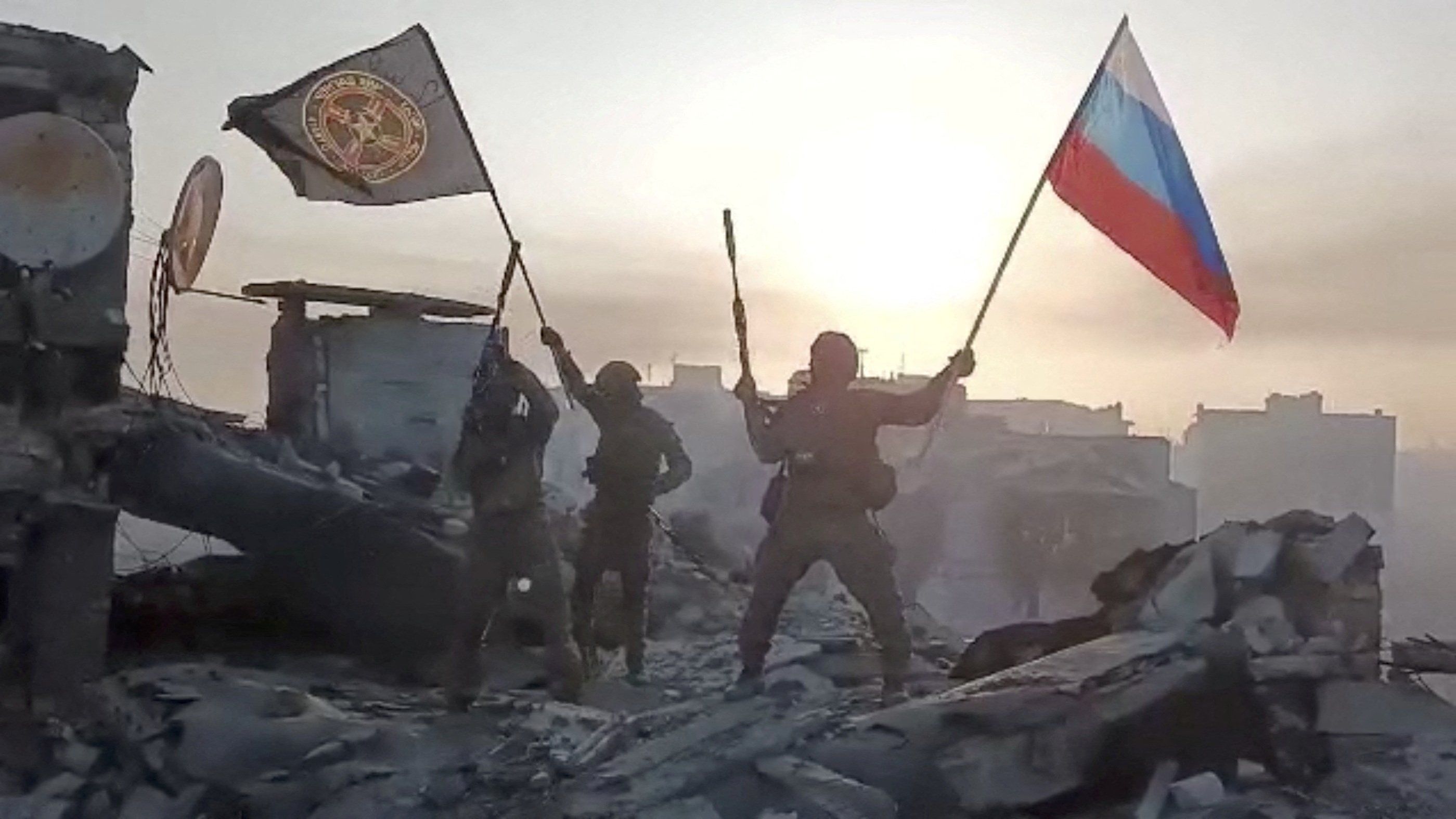 Wagner mercenary group fighters wave flags of Russia and Wagner group on top of a building 