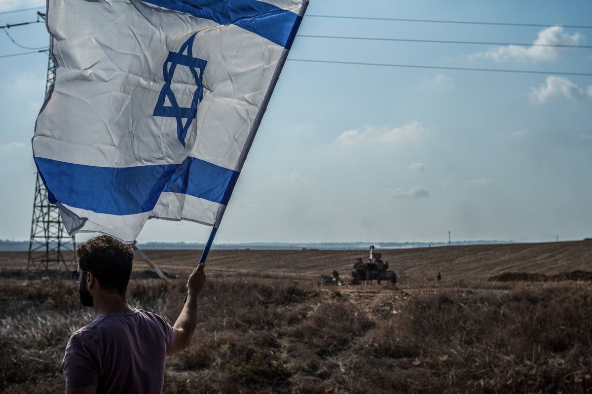 Man holding Israeli flag against the backdrop of an Israel Defense Forces tank. 