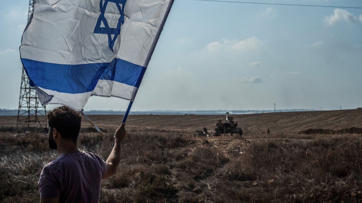 Man holding Israeli flag against the backdrop of an Israel Defense Forces tank.