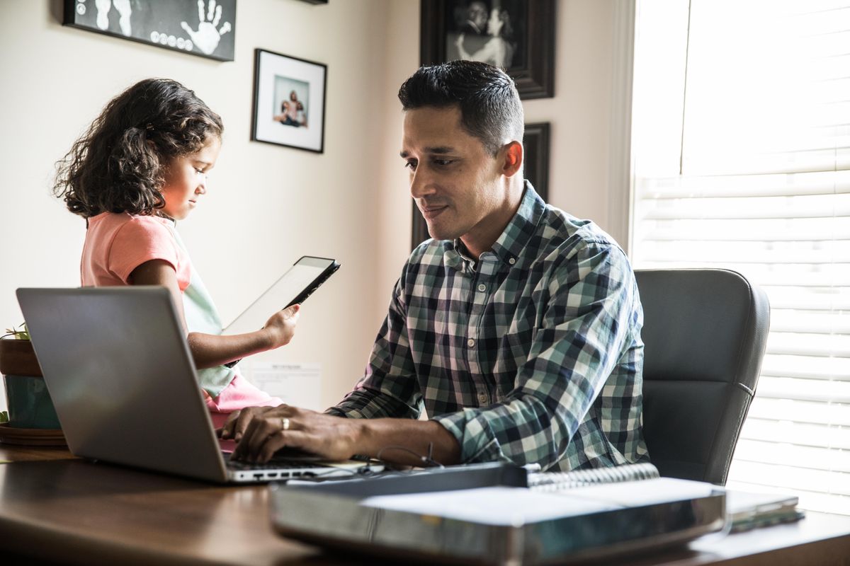 Man typing on a computer, next to a young child using a tablet.