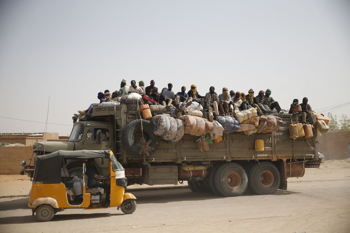 Migrants sit on their belongings in the back of a truck 