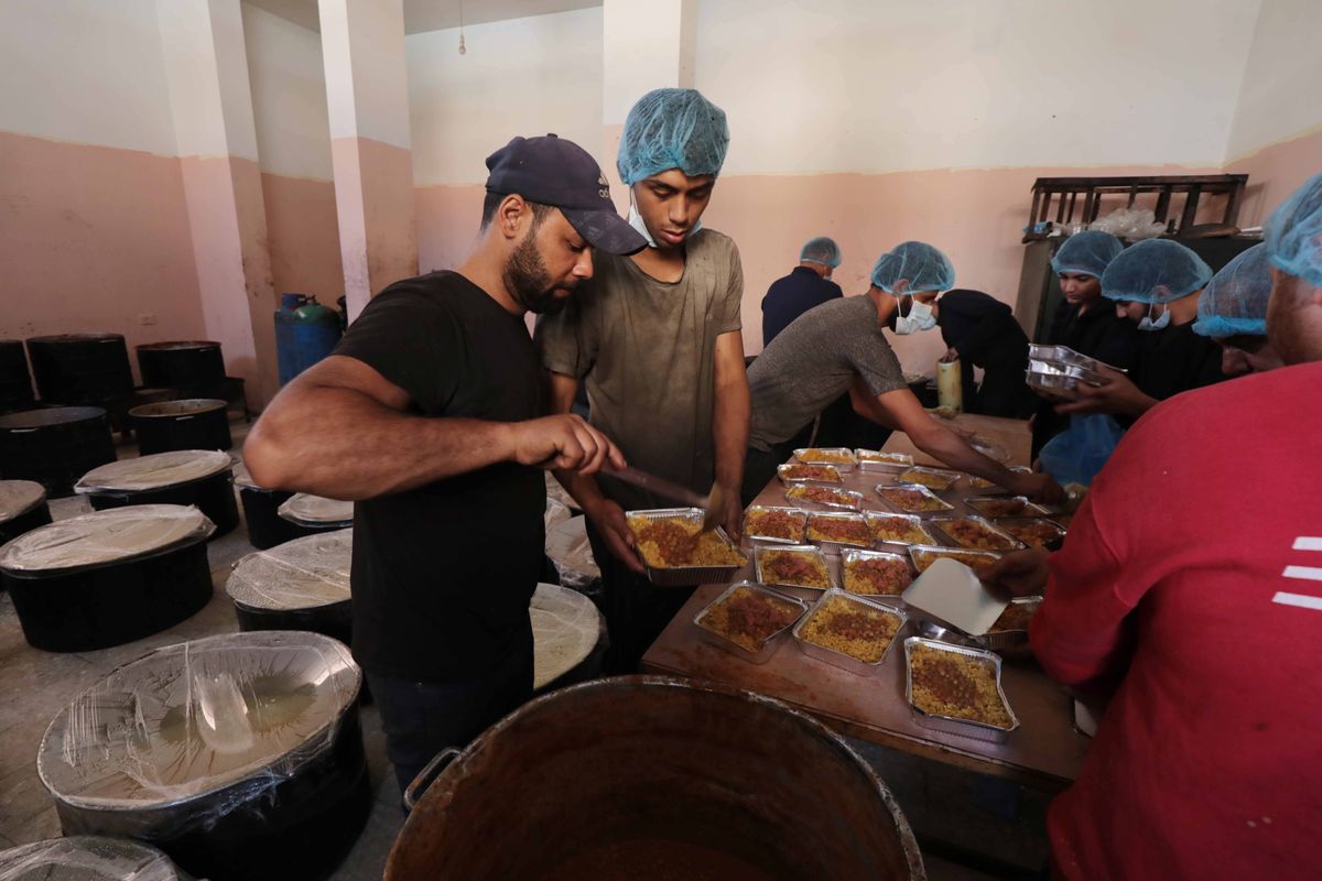 Palestinian people holding empty bowls try to reach out for food distributed by UNRWA workers at donation point