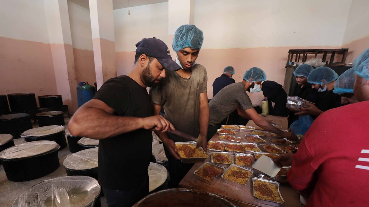 Palestinian people holding empty bowls try to reach out for food distributed by UNRWA workers at donation point