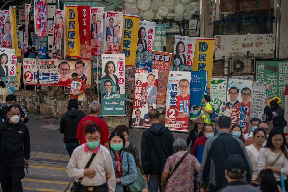 People are crossing the road in front of banners for a candidate of the 2023 District Council Election in Hong Kong, China, on December 10, 2023. This is the first district council election since the government introduced a new electoral system. (Photo by Vernon Yuen/NurPhoto)