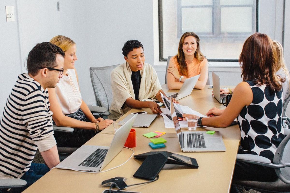 People gathering at a workspace with their laptops, speaking to each other. 