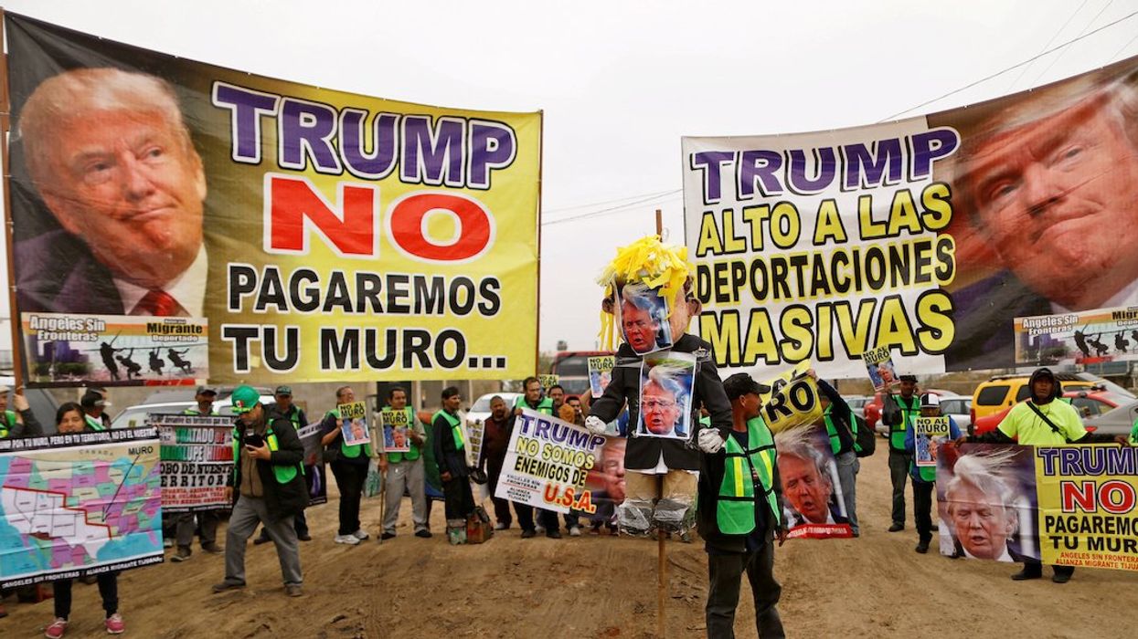 People hold signs reading "Trump, we will not pay for the wall" and "Trump, stop the mass deportations" near the border fence between Mexico and the U.S., in Tijuana, Mexico March 13, 2018.
