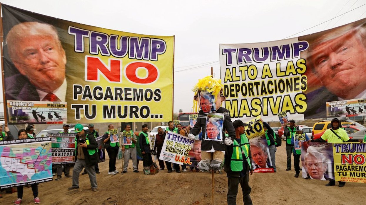 People hold signs reading "Trump, we will not pay for the wall" and "Trump, stop the mass deportations" near the border fence between Mexico and the U.S., in Tijuana, Mexico March 13, 2018.