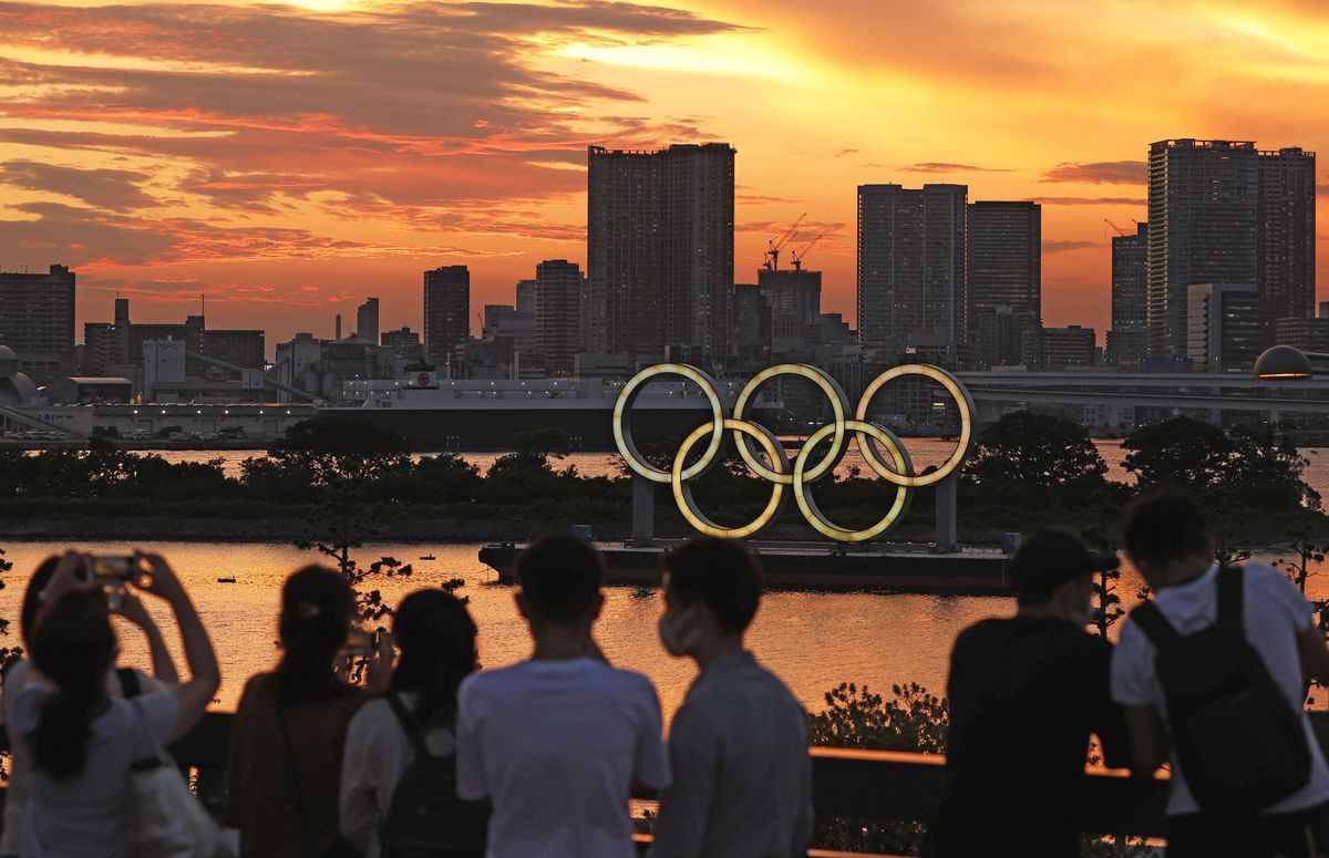 People look at an Olympics rings monument lit up after sunset in Tokyo on July 21, 2021, two days ahead of the Tokyo Olympics opening ceremony.