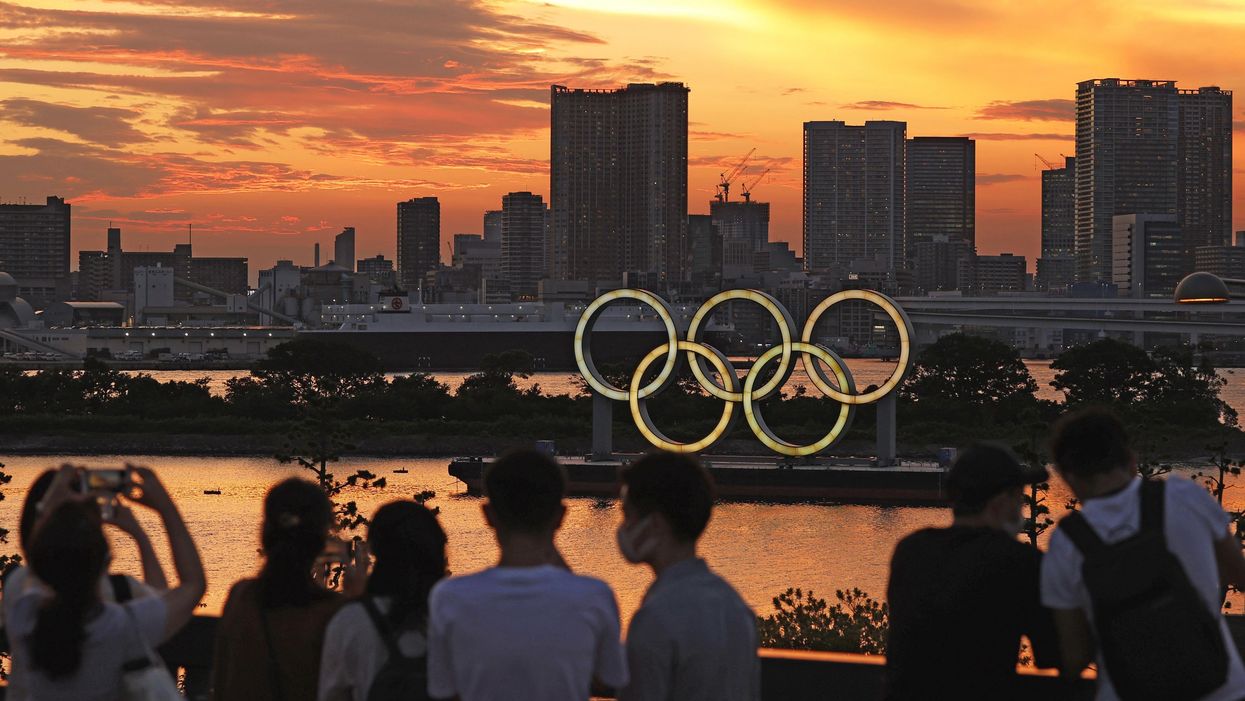 People look at an Olympics rings monument lit up after sunset in Tokyo on July 21, 2021, two days ahead of the Tokyo Olympics opening ceremony.