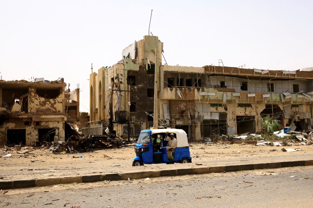 People pass by damaged cars and buildings at Khartoum's central market after clashes between the army and the paramilitary Rapid Support Forces. 