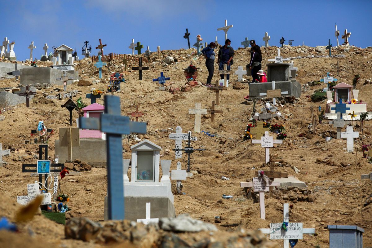 People stand among graves of victims of the coronavirus disease (COVID-19), and of others, at the municipal cemetery No. 12 in Tijuana, Mexico May 21, 2021