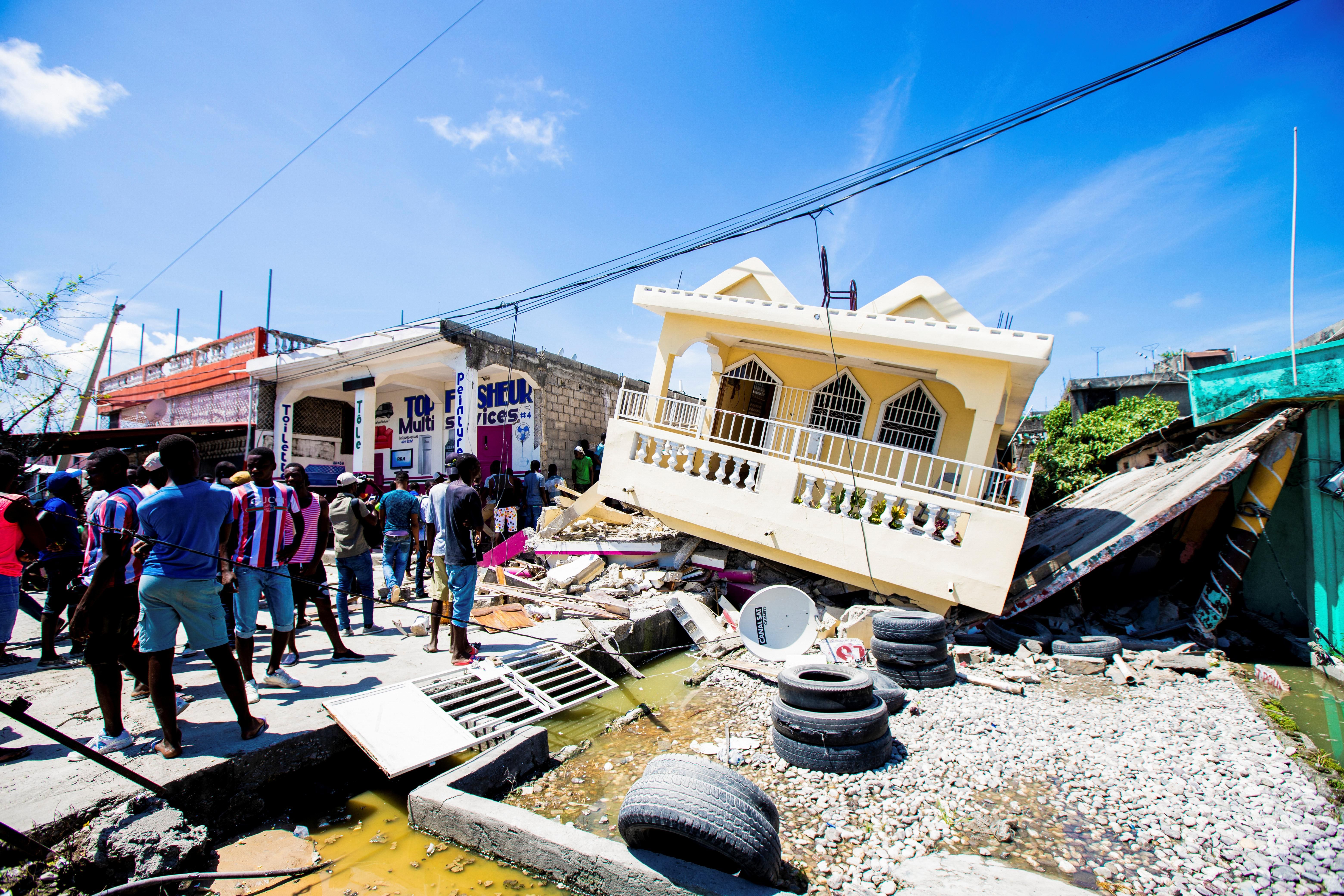 People stand next to a house destroyed following a 7.2 magnitude earthquake in Les Cayes, Haiti August 14, 2021.