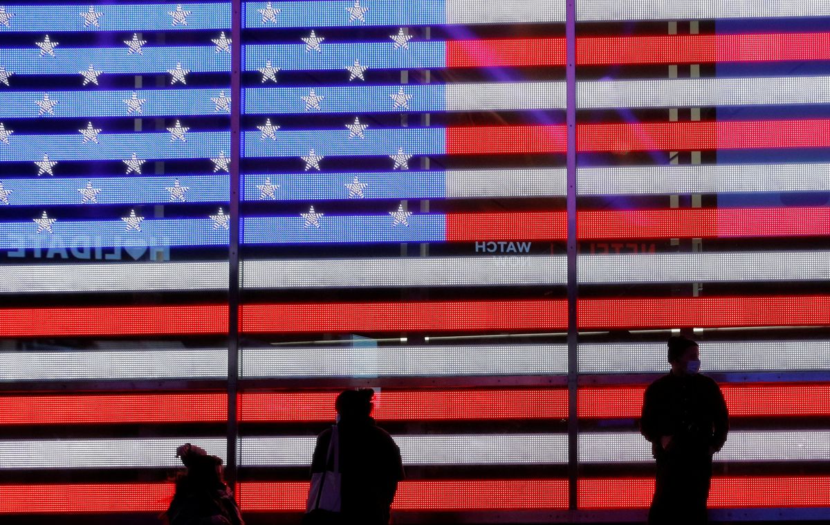 People stand next to a screen displaying a U.S. flag in Times Square during the 2020 U.S. presidential election in New York City, New York, U.S. November 4, 2020.