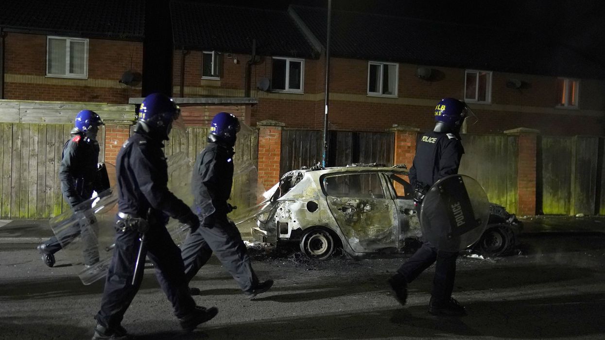 Police Officers walk past a burnt out police vehicle as they are deployed on the streets of Hartlepool following a violent protest.