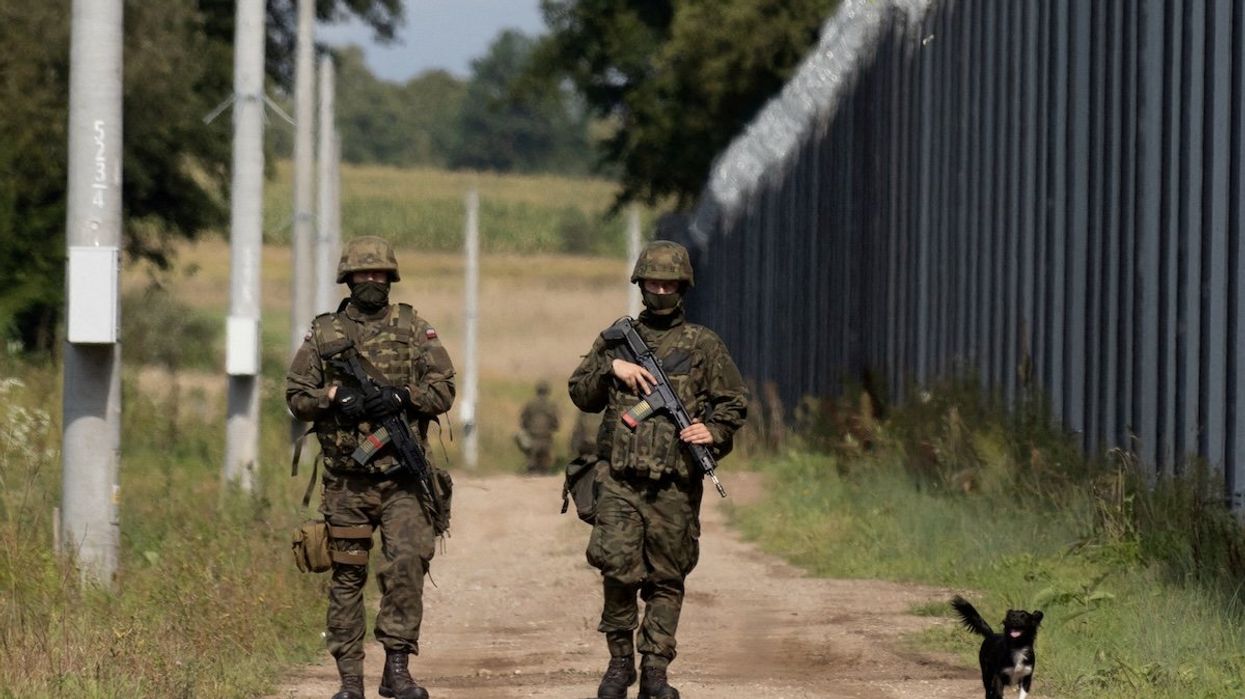 Polish soldiers and a local dog walk along the border fence on the Polish-Belarusian border in Usnarz Gorny, Poland.