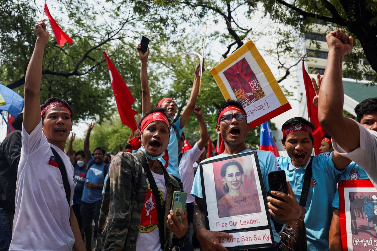 Protesters hold up a portrait of Aung San Suu Kyi and raise three-finger salutes