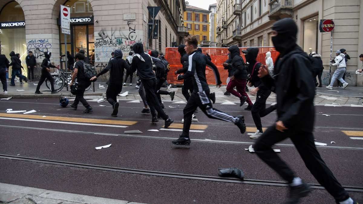 Protesters run along a street strewn with debris during a protest over the state of public services and the rising cost of living in Milan, Italy, October 18, 2026.