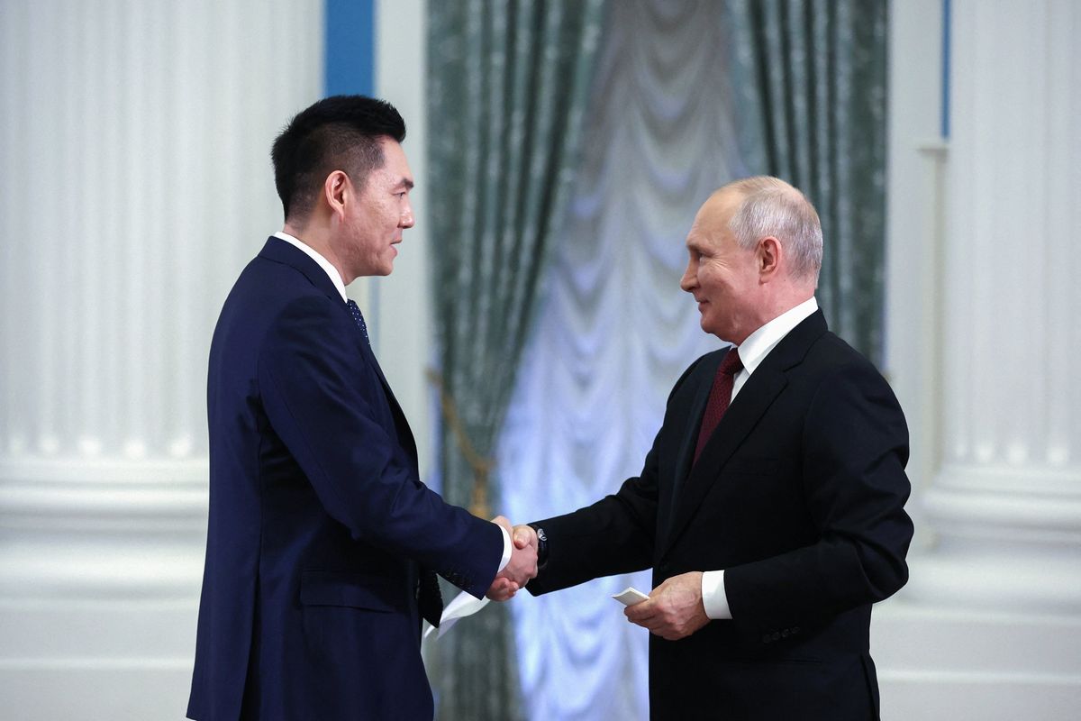 Russian President Vladimir Putin shakes hands with China Media Group anchor Wang Guan