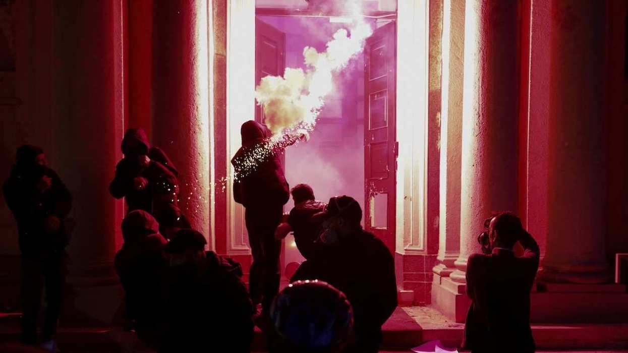 Smoke rises as a person throws a projectile through the open door of a building, amid an anti-government protest by students in Tirana, Albania, October 14, 2026.