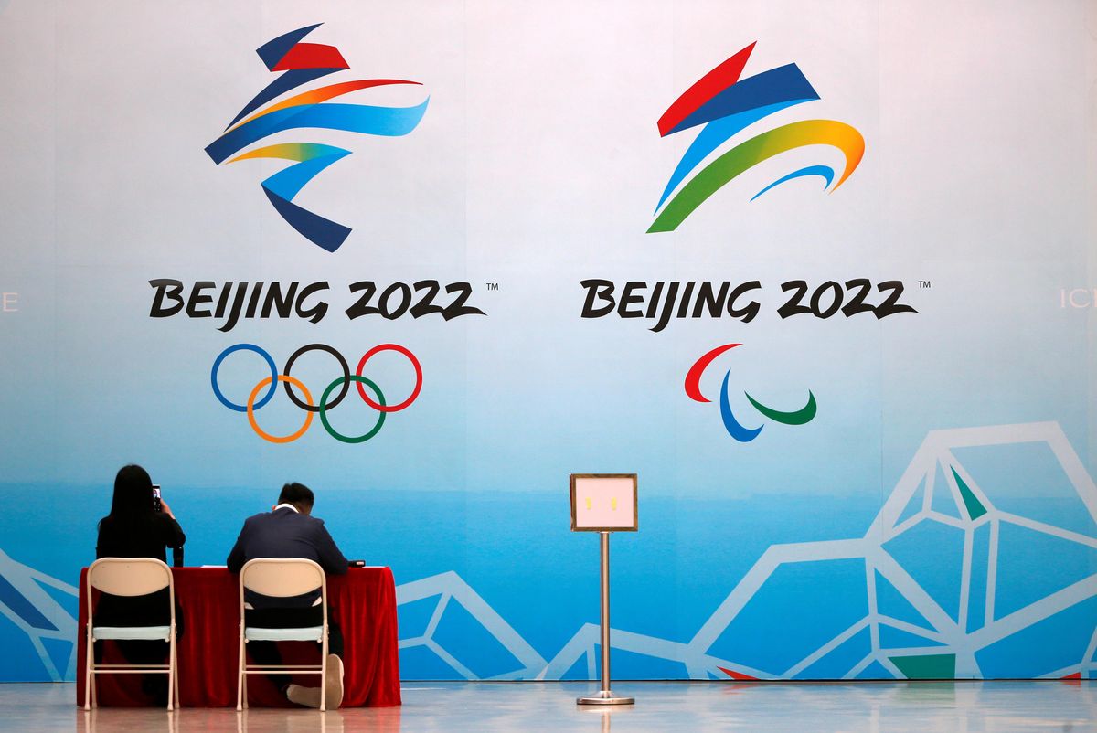 Staff members sit near a board with signs of the 2022 Olympic Winter Games, at the National Aquatics Center, known colloquially as the "Ice Cube", in Beijing, China April 1, 2021