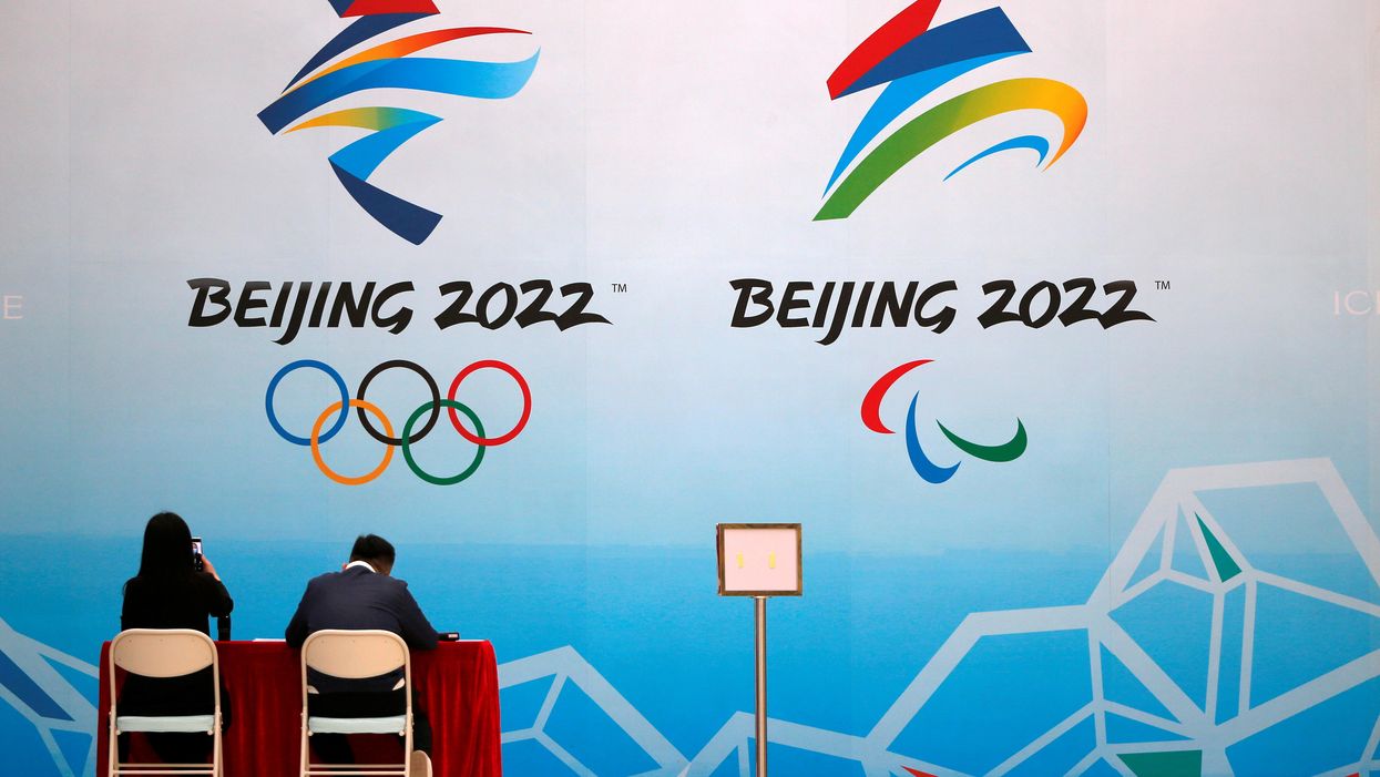 Staff members sit near a board with signs of the 2022 Olympic Winter Games, at the National Aquatics Center, known colloquially as the "Ice Cube", in Beijing, China April 1, 2021
