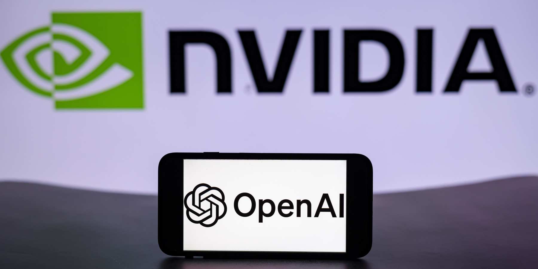 The logo of OpenAI is seen displayed on a mobile phone screen with the Nvidia logo in the background.