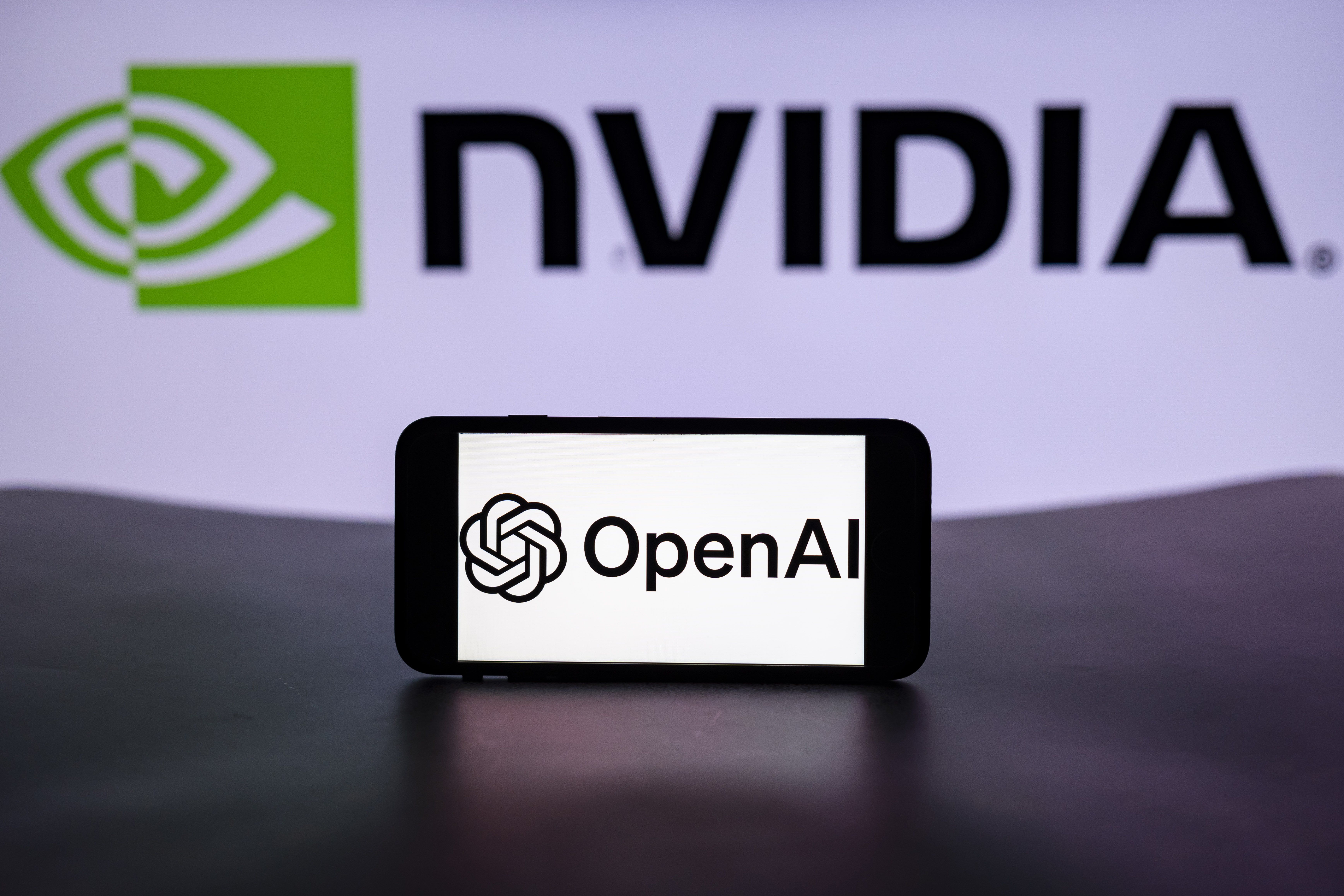 The logo of OpenAI is seen displayed on a mobile phone screen with the Nvidia logo in the background.