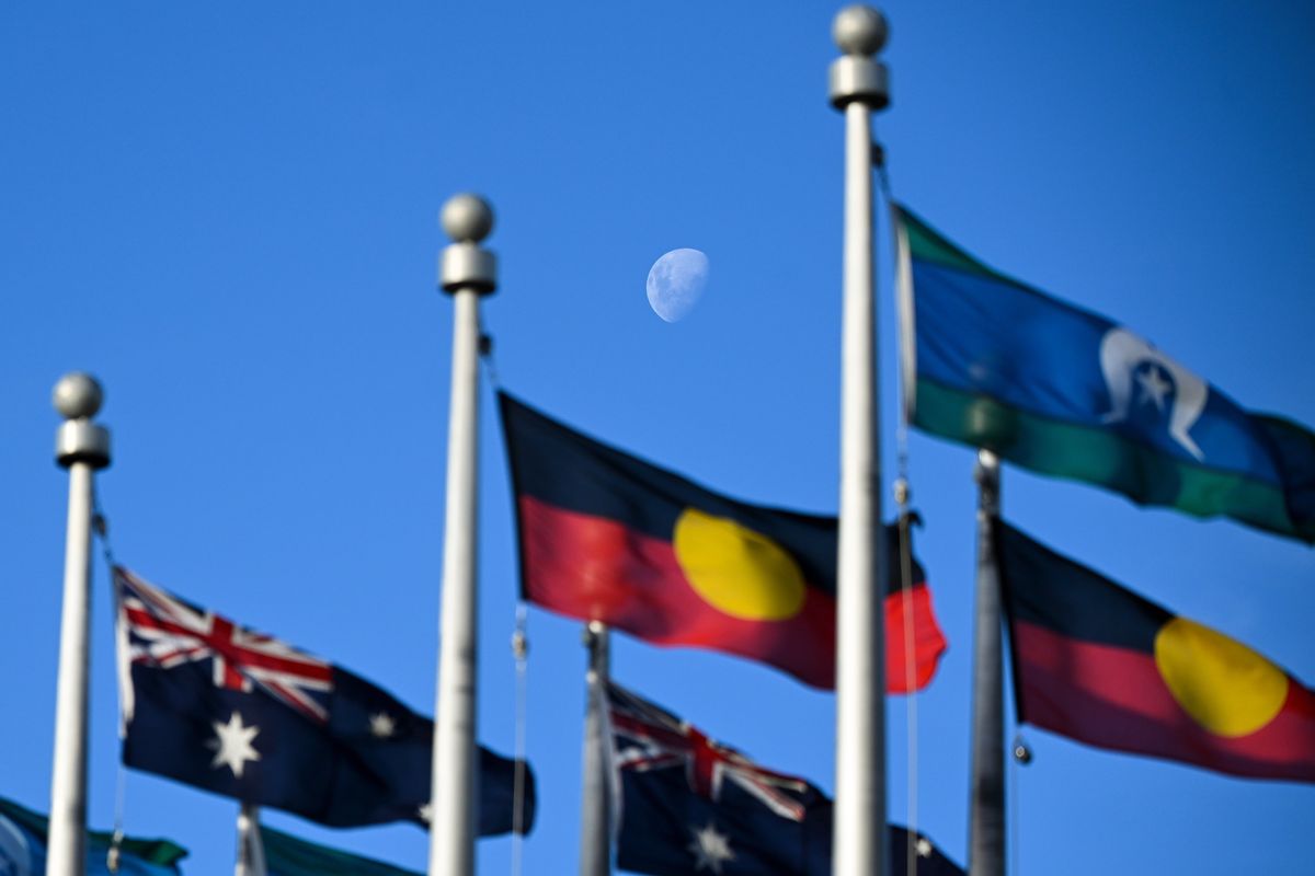 The moon is seen behind the Australian flag, the Aboriginal flag, and the flag of the Torres Strait Islands flying outside Parliament House in Canberra.