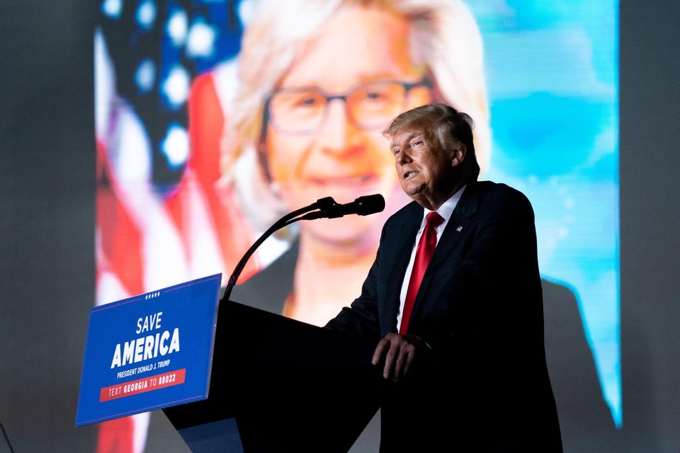 Trump speaks at a rally as a photo of Rep. Liz Cheney is projected on a screen.