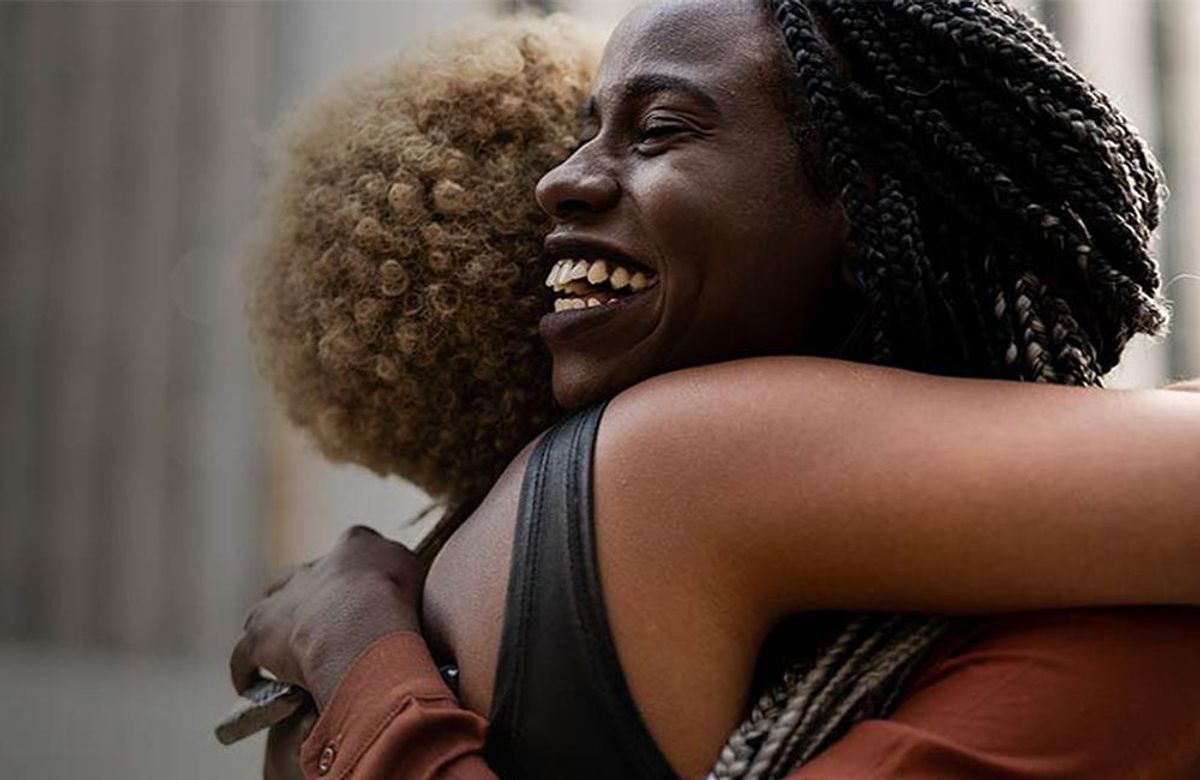 Two Black women hugging, with one woman pictured smiling