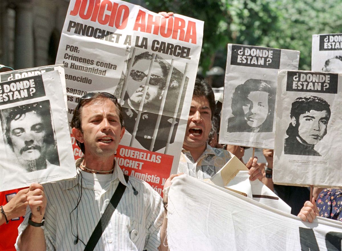 Two Chilean men yell slogans against former leader Gen. Augusto Pinochet while holding onto pictures of people allegedly disappeared during the dictatorship. 
