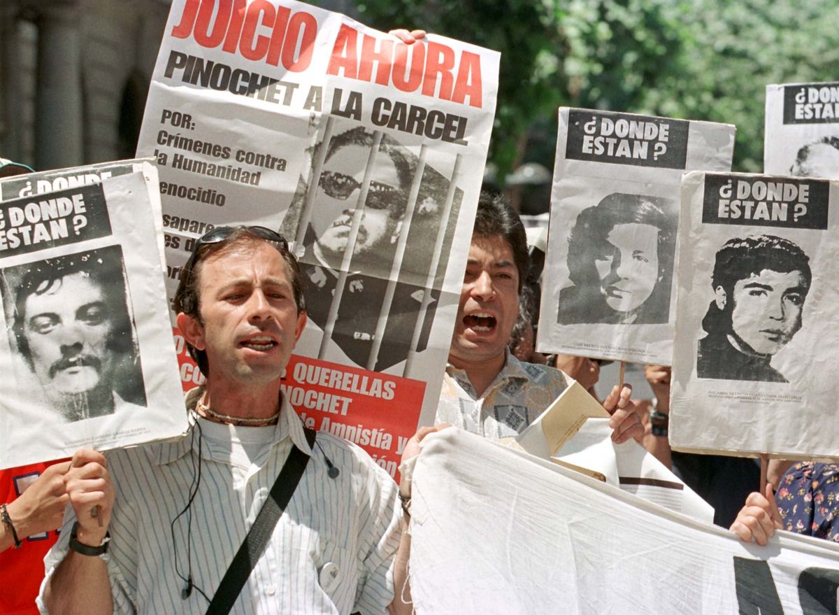 Two Chilean men yell slogans against former leader Gen. Augusto Pinochet while holding onto pictures of people allegedly disappeared during the dictatorship.