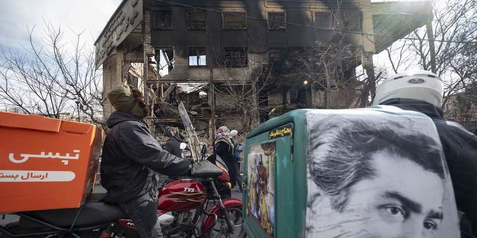 Two Iranian motorcyclists stop in front of the burned East Tehran General Directorate of Tax Affairs headquarters in Tehran, Iran, on January 21, 2026.