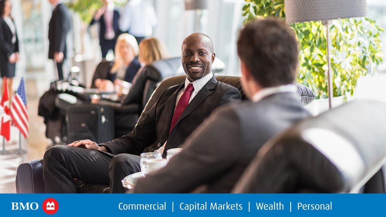Two men wearing suits sit in lobby armchairs for a meeting.