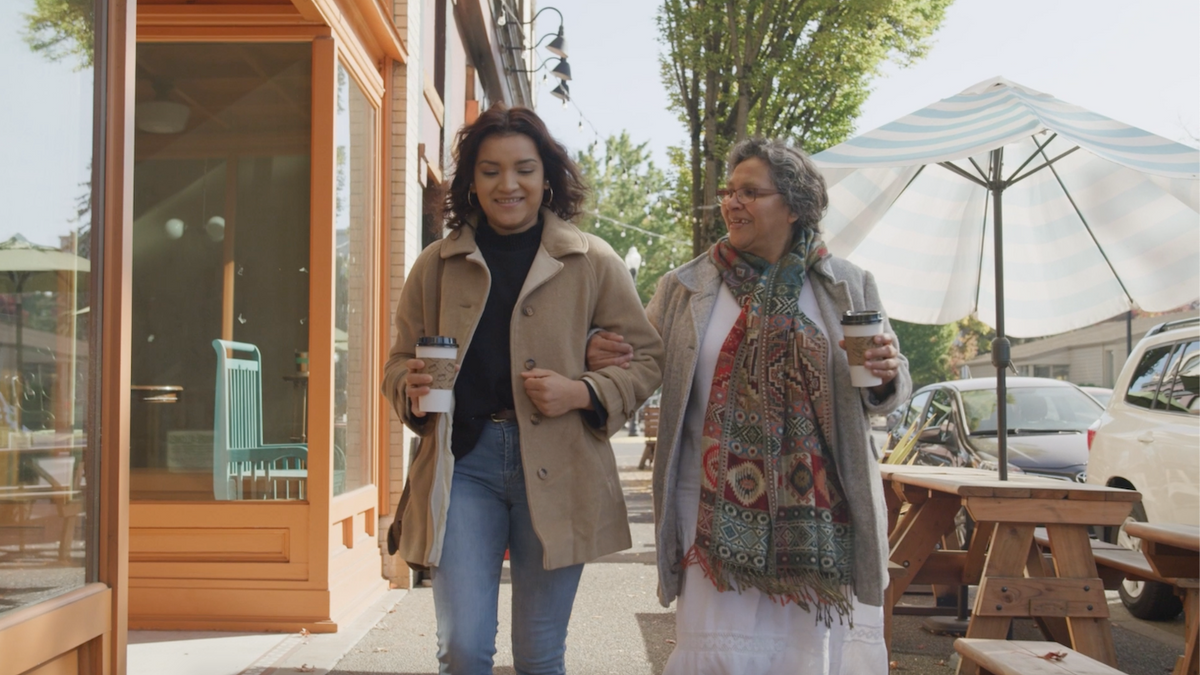 Two women holding cups of coffee, walking while they smile.