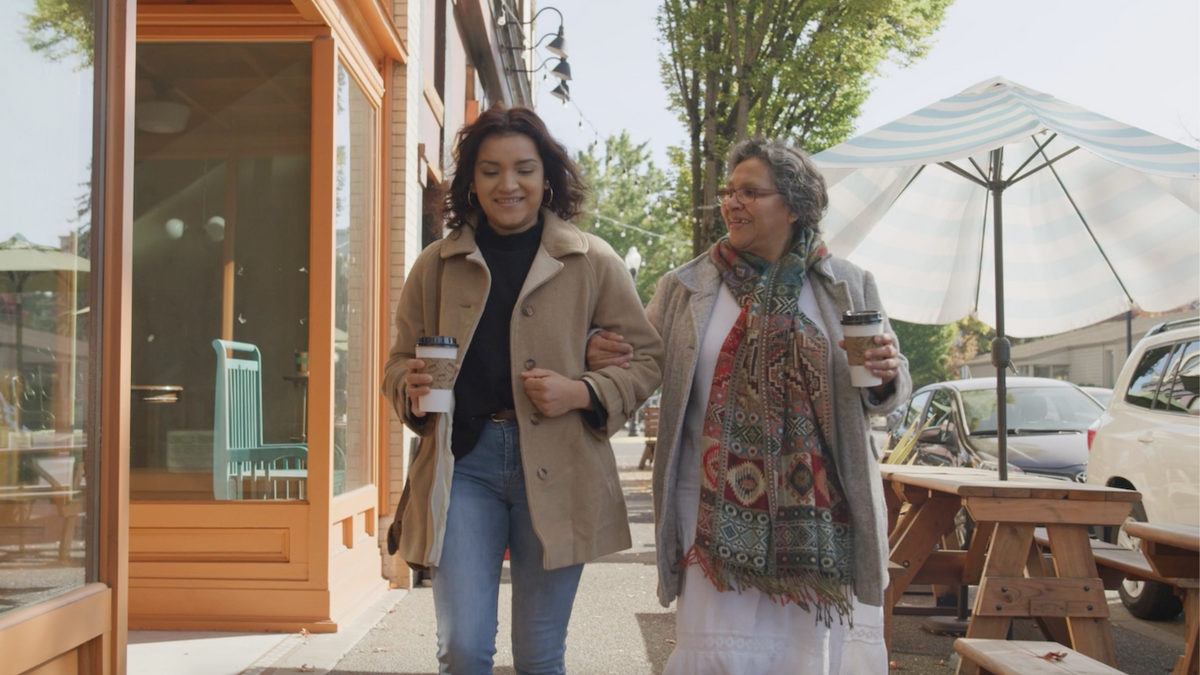 Two women holding cups of coffee, walking while they smile. 