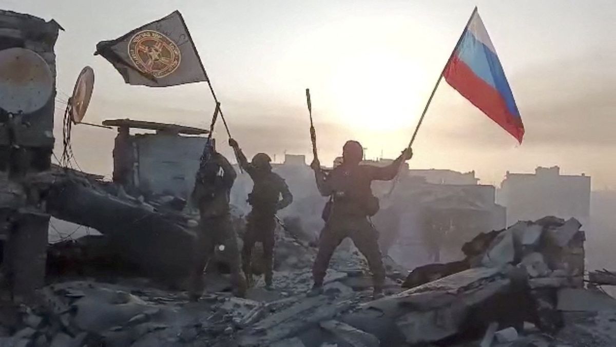 Wagner mercenary group fighters wave flags of Russia and Wagner group on top of a building 