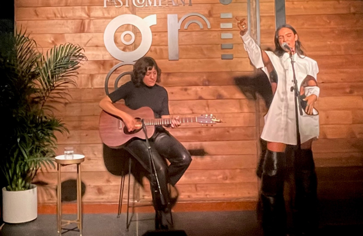 Woman playing the guitar, while another woman sings.